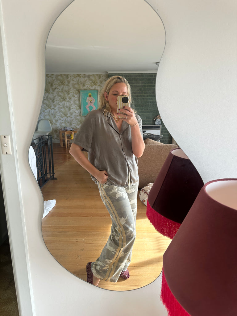 Person taking a mirror selfie in a room with a wooden floor and white walls.